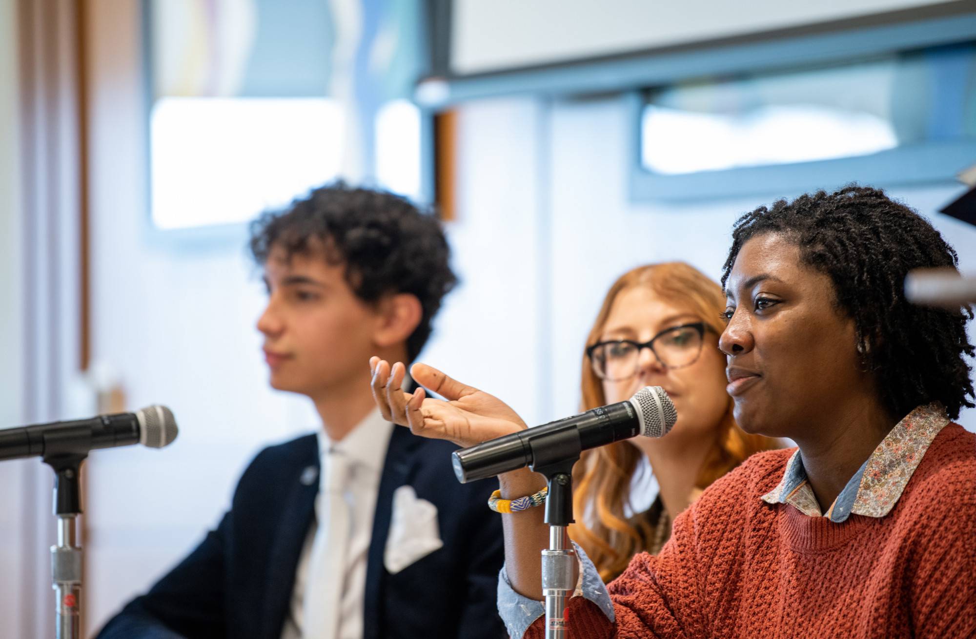 Three students sitting at a panel table answering questions; female student in foreground